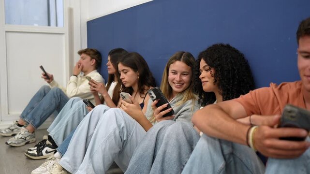 Diverse group of bored millennial and gen z friends sitting on the floor, each one engrossed in their own smartphone, showcasing digital addiction and lack of real life social interaction