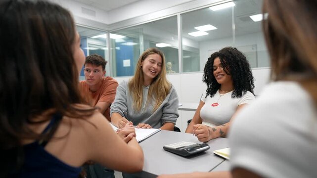 Multiethnic group of happy young students working together on a project, sharing ideas, laughing, and enjoying their collaborative learning experience inside a modern university classroom