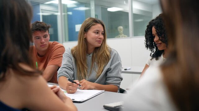 Diverse group of college students seated at a table, collaborating on an assignment, brainstorming ideas, taking notes and communicating effectively in a modern classroom setting