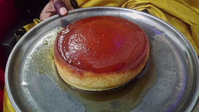 A video of an Indian saree-clad woman holding a caramel flan dessert, showing its smooth texture