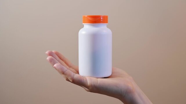Woman hand holding white supplement bottle against neutral beige background. Supplement packaging mockup supports healthcare branding, wellness promotion, product presentation, nutrition marketing