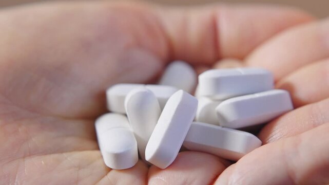 White oval pills in woman hand close up showing vitamins and dietary supplements for everyday wellness. Health support concept for preventive care, healthy habits, nutrition balance and self-care.