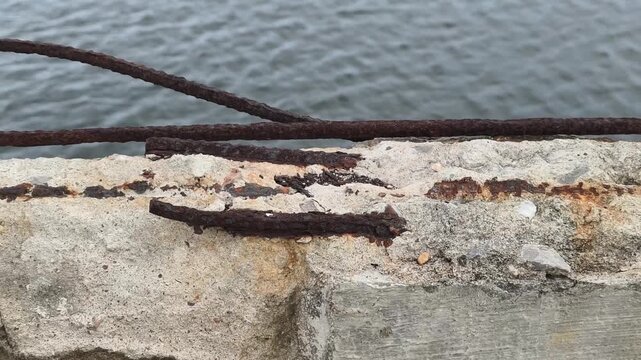Crumbling concrete exposes rusted rebar over a body of water