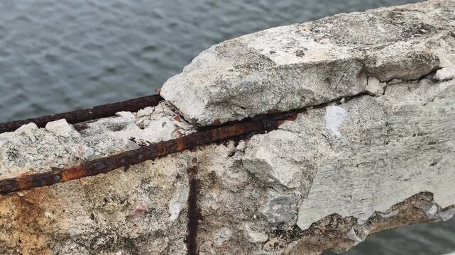 Crumbling concrete exposes rusted rebar over a body of water