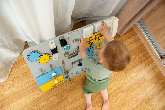 Toddler twisting locks and latches on sensory board. Age appropriate learning toy. Child discovering how everyday objects work. Motor skills training while having fun