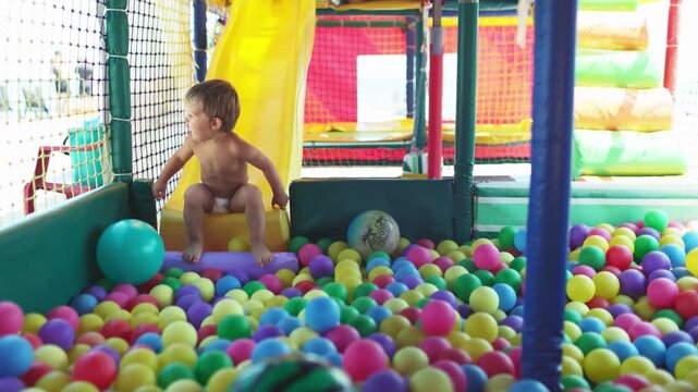 The kid plays in the playroom and rolls down the slide into the pool with small balls