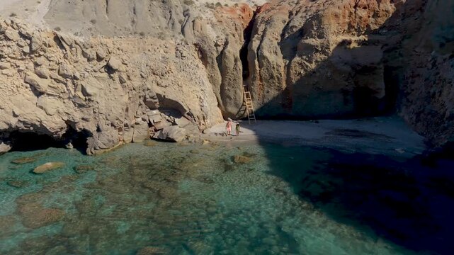 A couple of men and women walk at the Tsigrado Beach, Milos, Greece, where sunlit cliffs meet serene waters. Visitors can relax on pristine beaches and enjoy endless summer adventures