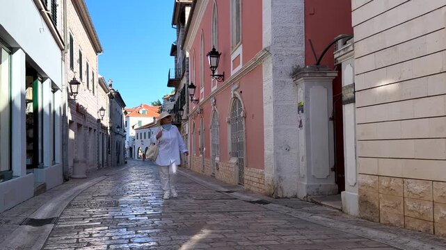 Senior Woman Walking in Historic Mediterranean Town. Senior woman walking along a quiet street in a historic Mediterranean town. Mature tourist enjoying travel, sightseeing and active retirement.