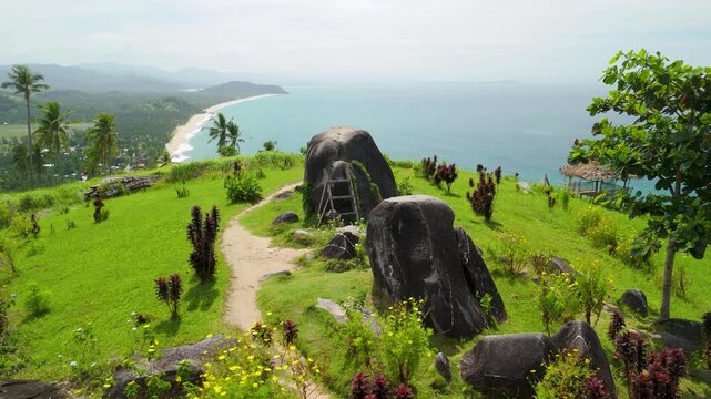 Aerial parallax over Bato ni Ningning sacred hilltop boulders with winding path and panoramic turquoise bay view in Philippines