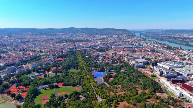 4K aerial drone footage over Vienna, Austria. Prater park with tree-lined Hauptallee, Riesenrad, Donaukanal, WU Wien campus, and Danube River stretching to the Wienerwald.