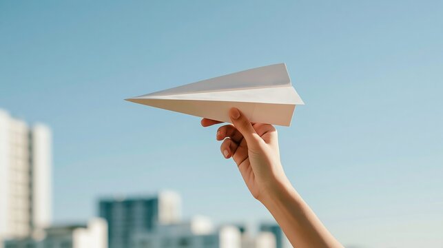 Hand holding paper airplane, launching dream for future, urban background, concepts of aspiration and freedom