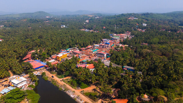 Aerial view of the coastal town with colorful rooftops nestled among dense palm trees and rolling hills Gokarna, Karnataka, India.