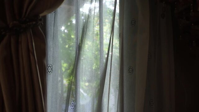 White sheer lace curtain with embroidered pattern hanging by the window in warm natural sunlight.