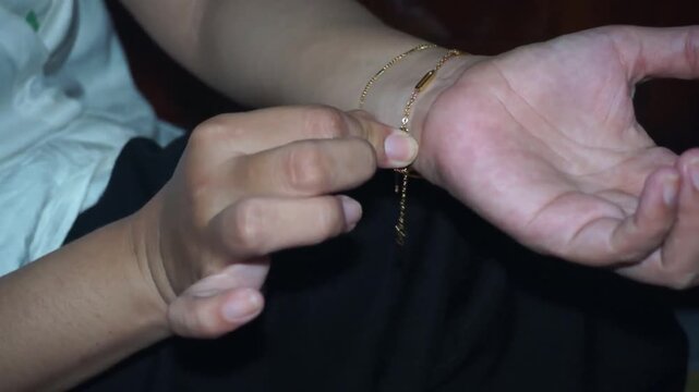 Close up of hands putting on and fastening delicate gold chain bracelet on wrist