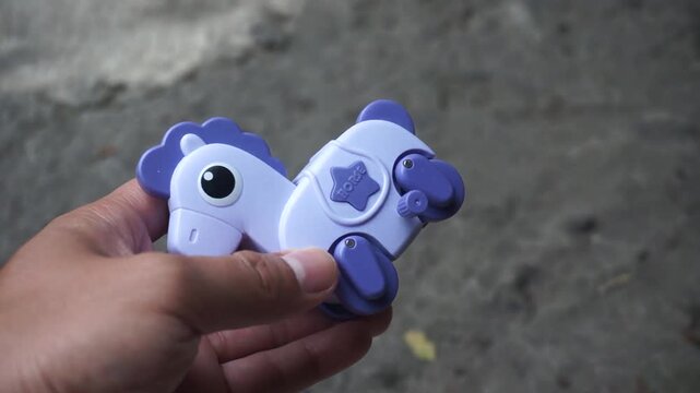 Hand holding a purple plastic wind-up horse toy outdoors