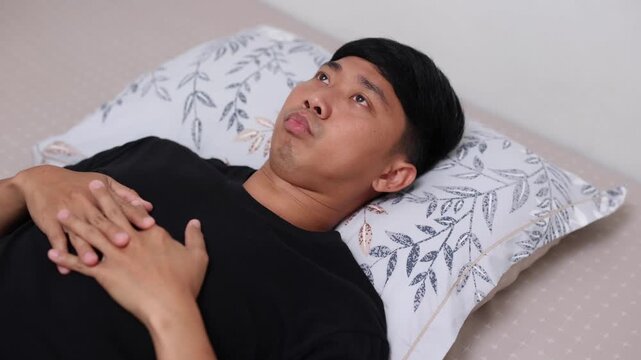 Depressed young man suffering from insomnia, lying awake in bed and touching his forehead with stress