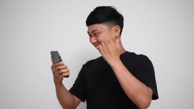 Young Asian man looking at his smartphone, smiling, celebrating success and raising fist happily