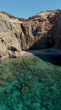 Discover the enchanting beauty of Tsigrado Beach, Milos, Greece,, as vibrant turquoise waters meet majestic cliffs. Ideal for tranquility and adventure seekers, a couple walking on the beach