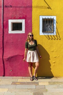 Young woman in front of colorful house, red and yellow house facade, Burano Island, Venice, Veneto, Italy