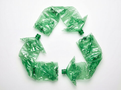 Wrinkled green plastic bottles create a recycling symbol on white, connecting discarded PET packaging with zero waste habits.