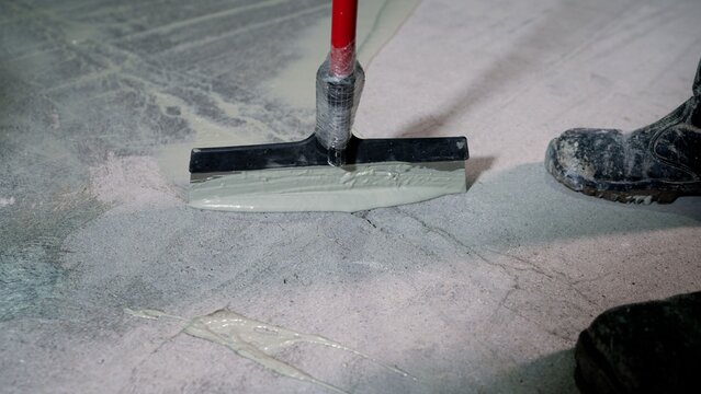 Construction worker applying epoxy resin coating to concrete floor with squeegee tool
