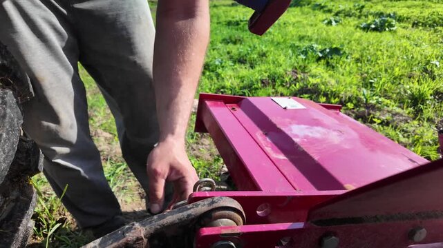 Slow motion close-up of a male operator using a hammer to install a spring locking pin into a tractor rear hitch connection on a rotary tillage implement. The pin is driven into place to secure the