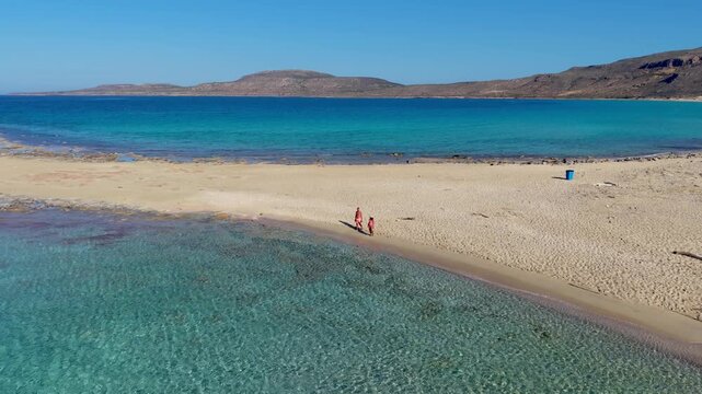 Enjoy a stunning view of Simos Beach in Elafonisos, Greece. Crystal clear waters meet golden sands as visitors stroll along the shoreline and soak up the sun. A perfect getaway for relaxation.