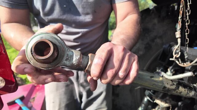Close-up and medium shots of a man manually loosening and adjusting a locking nut on a tractor rear linkage system. The sequence shows finger strain and mechanical effort while tightening and