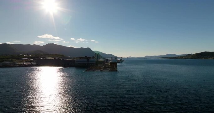 Drone view of coastal industrial park and fish farming infrastructure surrounded by ocean and mountains in Stokmarknes, Norway. Aerial forward, copy space