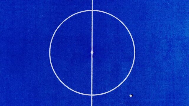 Aerial photograph of a blue artificial turf futsal field, with a white line down the center.