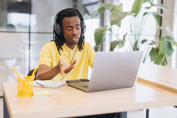 African american man having a virtual meeting on a laptop, working remotely with headphones in a modern office © anatoliycherkas