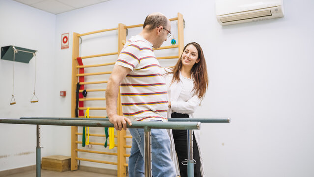 Physiotherapist assisting senior man with physical disability walking using parallel bars for rehabilitation training in a medical clinic