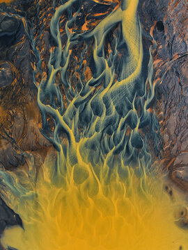Aerial view of intricate braided glacial river channels with yellow sediment and dark volcanic silt in Hella, Rangarthing ytra, Iceland.