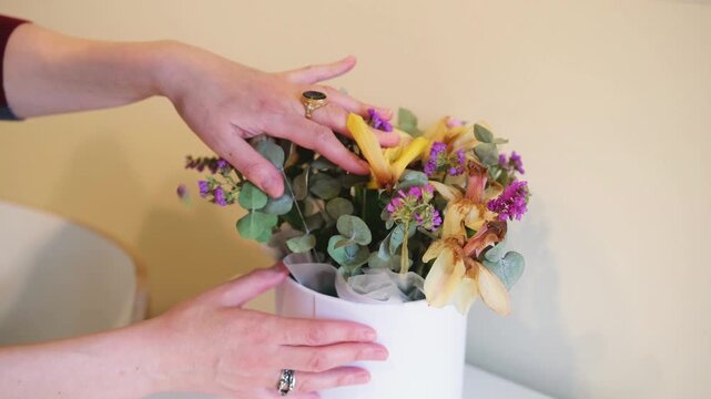 woman checks wilted bouquet and removes vase with flowers from table. fresh bouquet needs regular care to keep home clean and tidy. removing old bouquet is important daily home routine