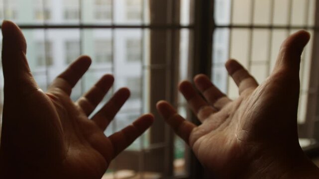 Two open hands palms facing up raised toward sunlight through window with warm golden backlight spiritual prayer concept