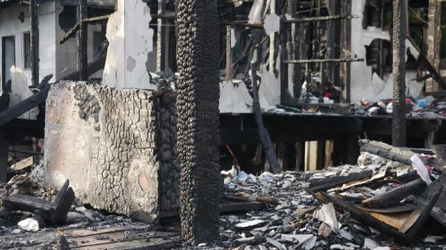 Fire disaster aftermath exterior view of burned destroyed residential house with charred wooden columns collapsed structure and debris