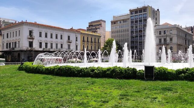 A picturesque view of the iconic fountain at Omonoia Square in Athens, Greece, surrounded by a harmonious mix of grand neoclassical facades and modern buildings under a clear blue sky.
