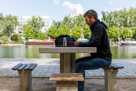 Un homme assis &agrave; une table en train d'utiliser un smartphone, le long du canal de l'Ourcq &agrave; Paris