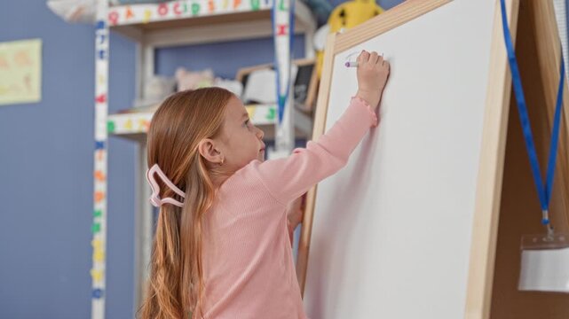 Girl writes with marker on whiteboard in classroom building, reaches up in pink sweater with hairclip and earring visible; concentration learning creativity.