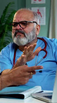 Indian male doctor using laptop while consulting young man patient as experienced physician discusses medical reports in modern Indian clinic OPD healthcare consultation