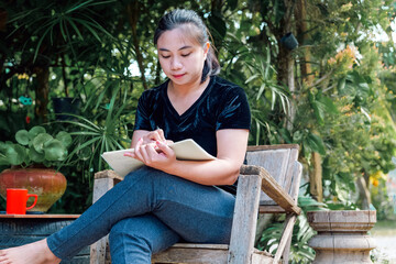 Naklejka premium Young Asian Woman Writing in Notebook Outdoors