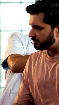 Indian male doctor treating patient during routine health checkup as experienced physician examines young man with stethoscope in modern Indian clinic OPD healthcare consultation visit