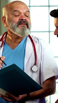Indian male doctor consulting male patient with medical report as experienced physician advises young man inside modern Indian clinic OPD healthcare consultation