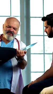 Indian male doctor consulting male patient with medical report as experienced physician advises young man inside modern Indian clinic OPD healthcare consultation