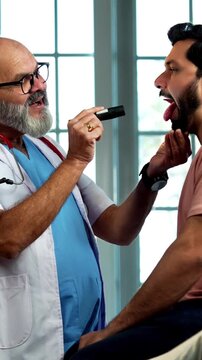 Indian male doctor checking male patient with torch during routine medical examination as experienced physician assesses young man inside modern Indian clinic OPD healthcare visit