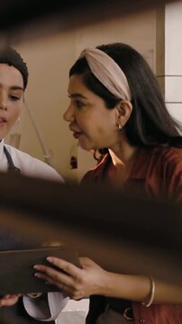 Vertical video: Taking tablet from lead, chef in coat tapping screen and reviewing menu in kitchen