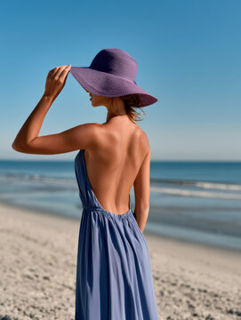 Woman backless dress purple hat beach sand ocean summer sunny day fashion style vacation