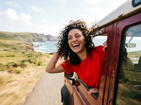 Woman laughing and enjoying a scenic road trip in a vintage vehicle, feeling the wind in her hair as she looks out at the stunning coastal landscape