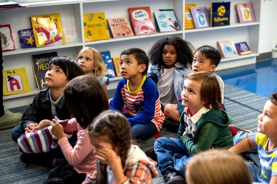 Diverse group of children sitting on the floor in a library setting.