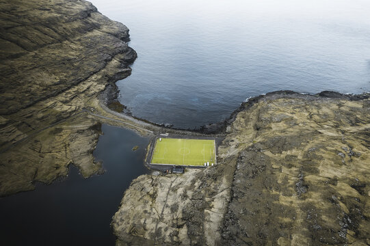Aerial view of the iconic Eidi football pitch surrounded by rugged cliffs and the dark waters of the Atlantic Ocean in the village of Eidi Faroe Islands.
